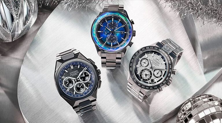 Luxury Gifts; Featuring an image of three ATTESA watch models on a silver background with holiday ornaments. Featuring ATTESA models CC4076-65A, AT8314-53L and CC4106-74E
