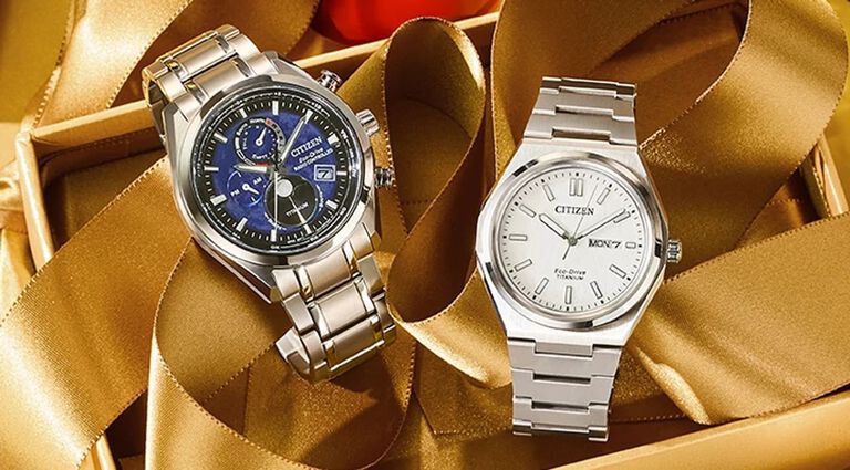 Images of two watches on top of gold holiday ribbon. Featuring Tsuki-yomi A-T watch model BY1010-57L and Zenshin Three-hand watch model AW0130-85A