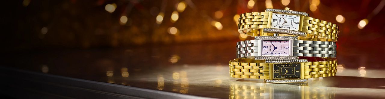 Women's Rectangular-Faced Watches; Image of three Petite Palidoro watch models EG7110-54Y, EG7112-59E and EG7112-59D on a table with holiday lights in the background