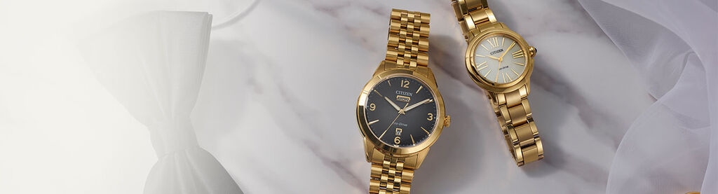 Wedding & Engagement Watch Gifts; Image of men's and women's watches sitting on a table with wedding rings, a tie and champagne glass. Featuring Rolan watch model AW0152-58H and Ceci watch model EM1162-52A