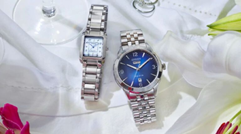 Wedding & Engagement Watch Gifts; Image of men's and women's watches sitting on a table with wedding rings and flowers. Featuring Rolan watch model AW0150-53L and Citizen L Bianca watch model EW5600-52D