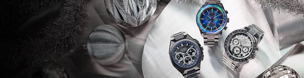 Luxury Gifts; Featuring an image of three ATTESA watch models on a silver background with holiday ornaments. Featuring ATTESA models CC4076-65A, AT8314-53L and CC4106-74E
