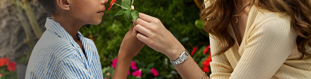 Mother wearing Citizen L Bianca watch EW5620-55A, sitting in a garden with her son smelling a flower.